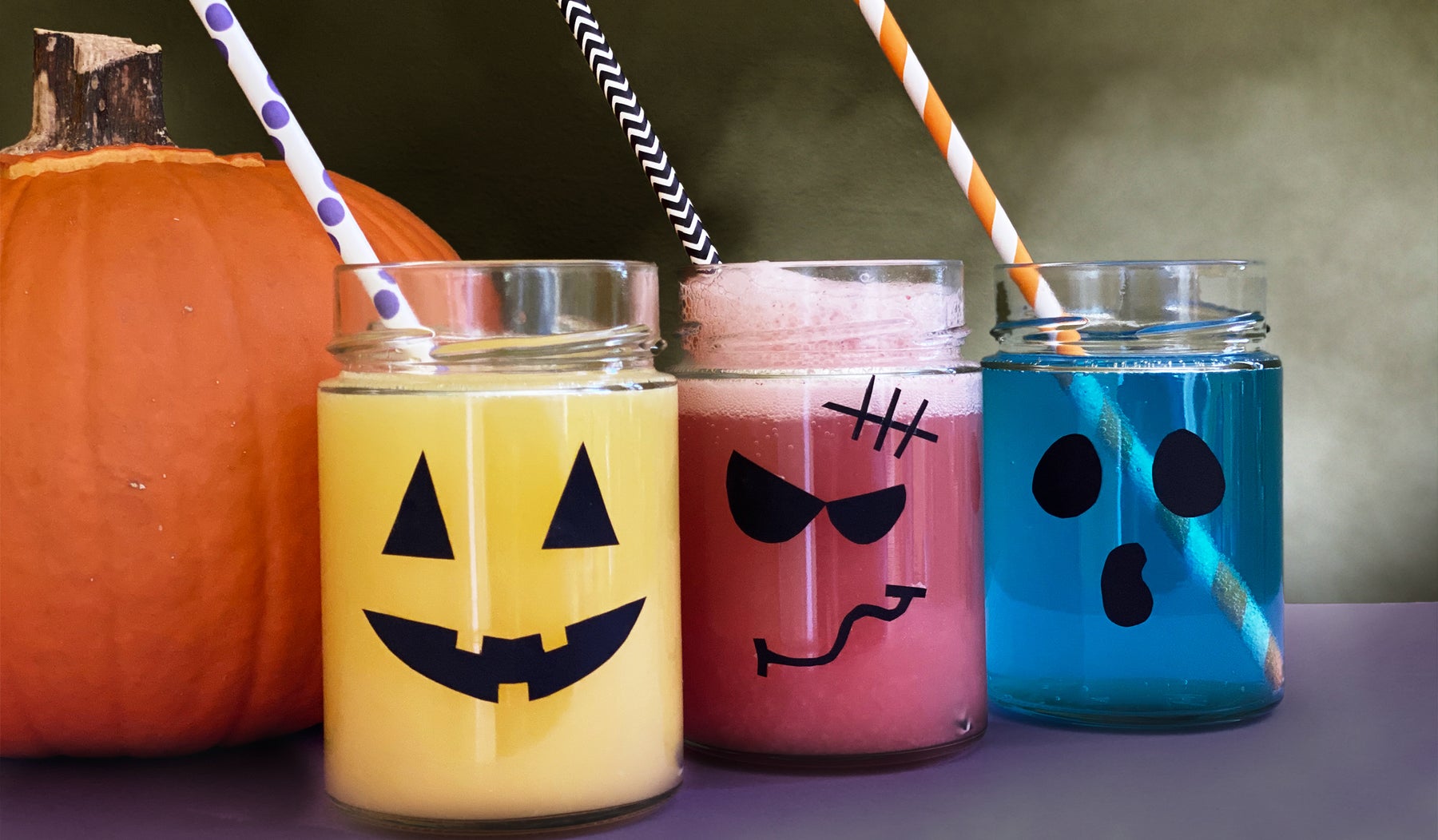 Three glass jars lined up containing drinks that are yellow, red, and blue.